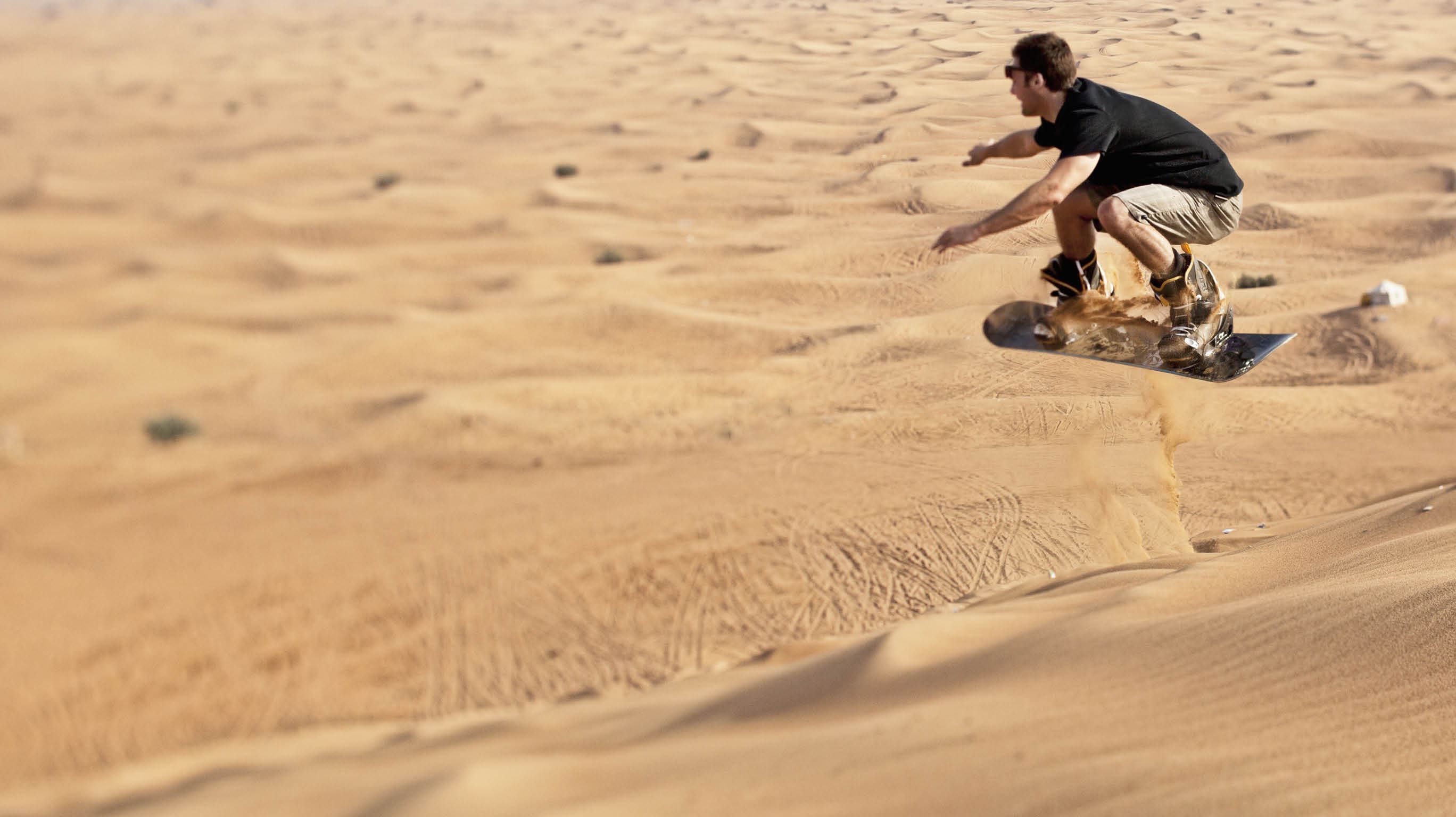 25 year old man sand boarding on the sand dune called Big Red in the desert near Dubai 