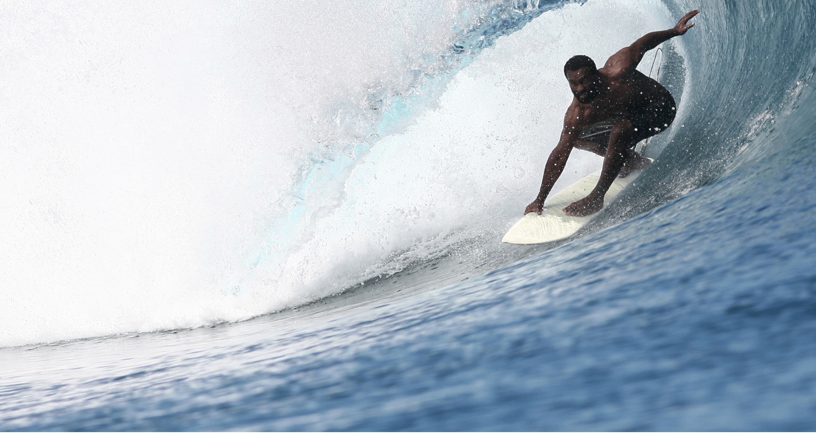 A fijian surfer rides under the lip of a breaking wave in Fiji