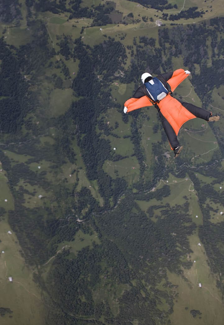 Wingsuit skydiver is tracking over green landscape