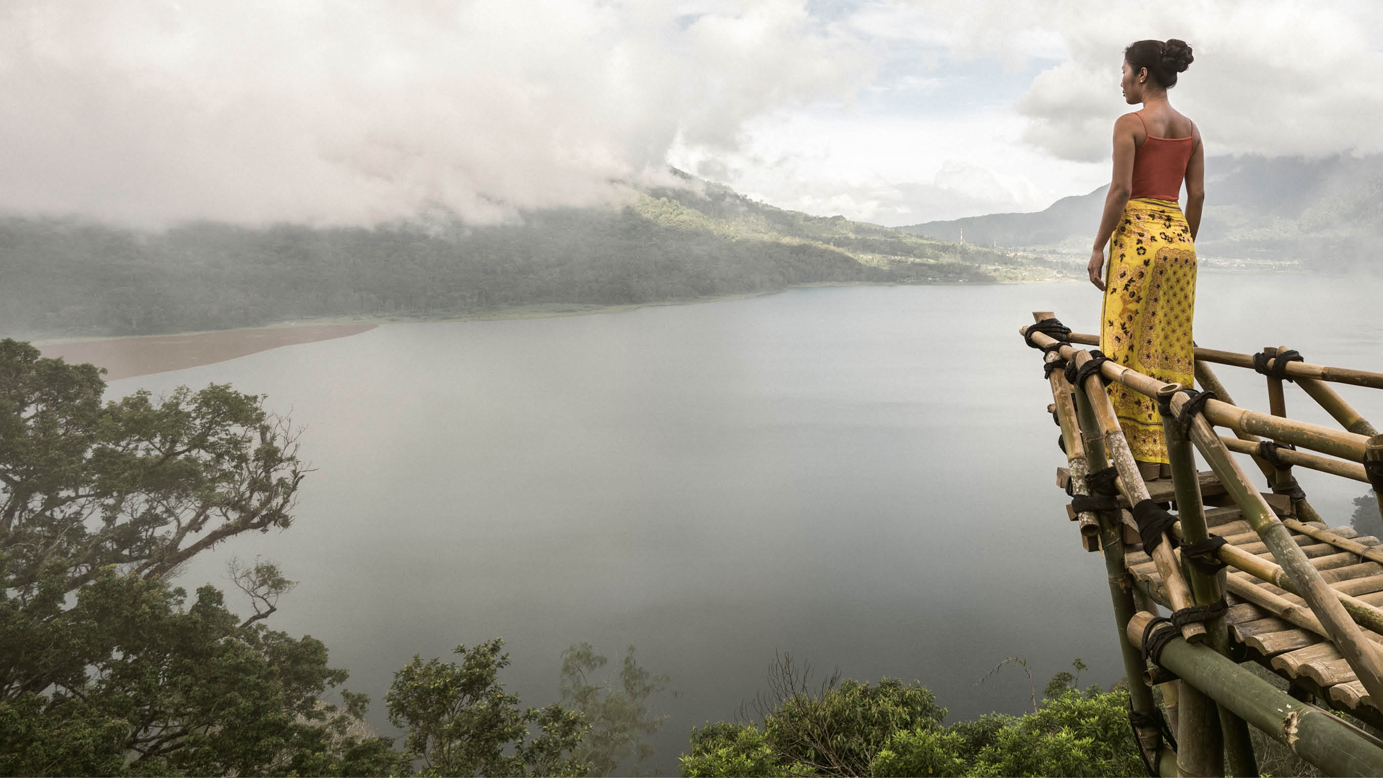 asia, indonesia, bali, an asian woman standing on a bamboo viewing platform, admiring the view of Danau Buyan lake below, through the clouds