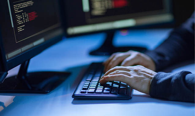 cybercrime, hacking and technology concept - hands of hacker in dark room writing code or using computer virus program for cyber attack