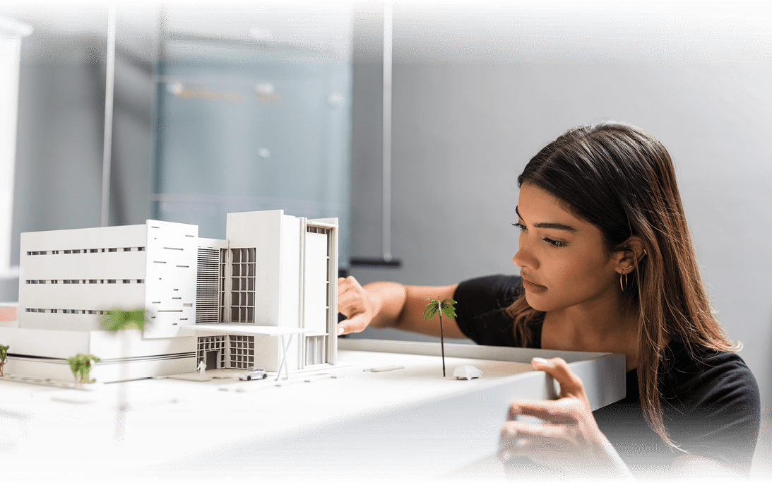 Young good looking female engineer analyzing model at desk in architect office