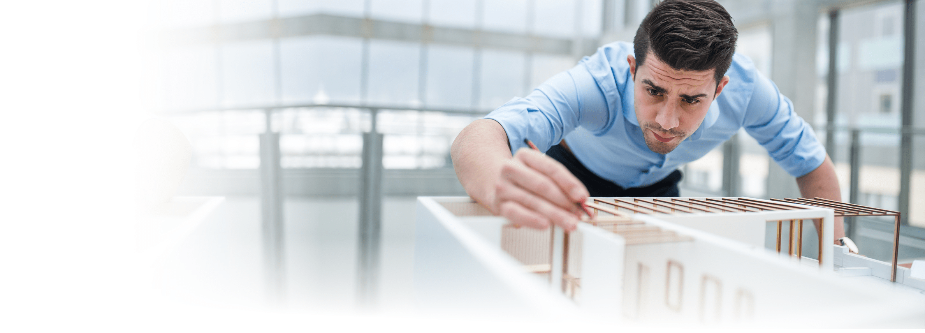 Young businessman or architect with model of a house standing at the desk in office, working 