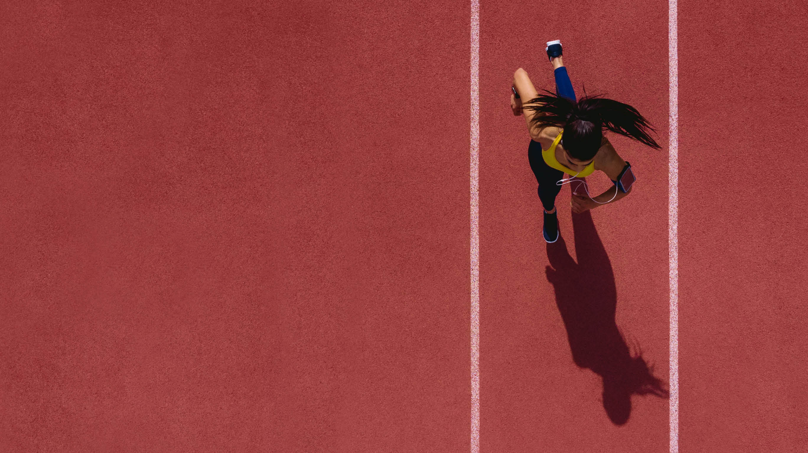 Young female professional athlete listening to music and training by sprinting on running track