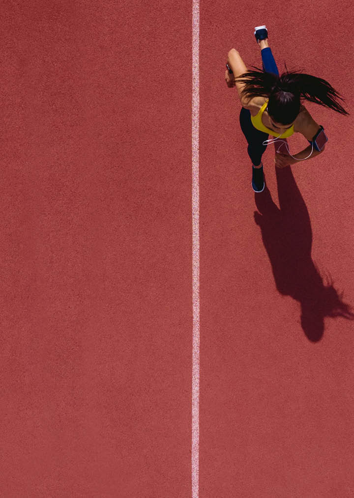 Young female professional athlete listening to music and training by sprinting on running track