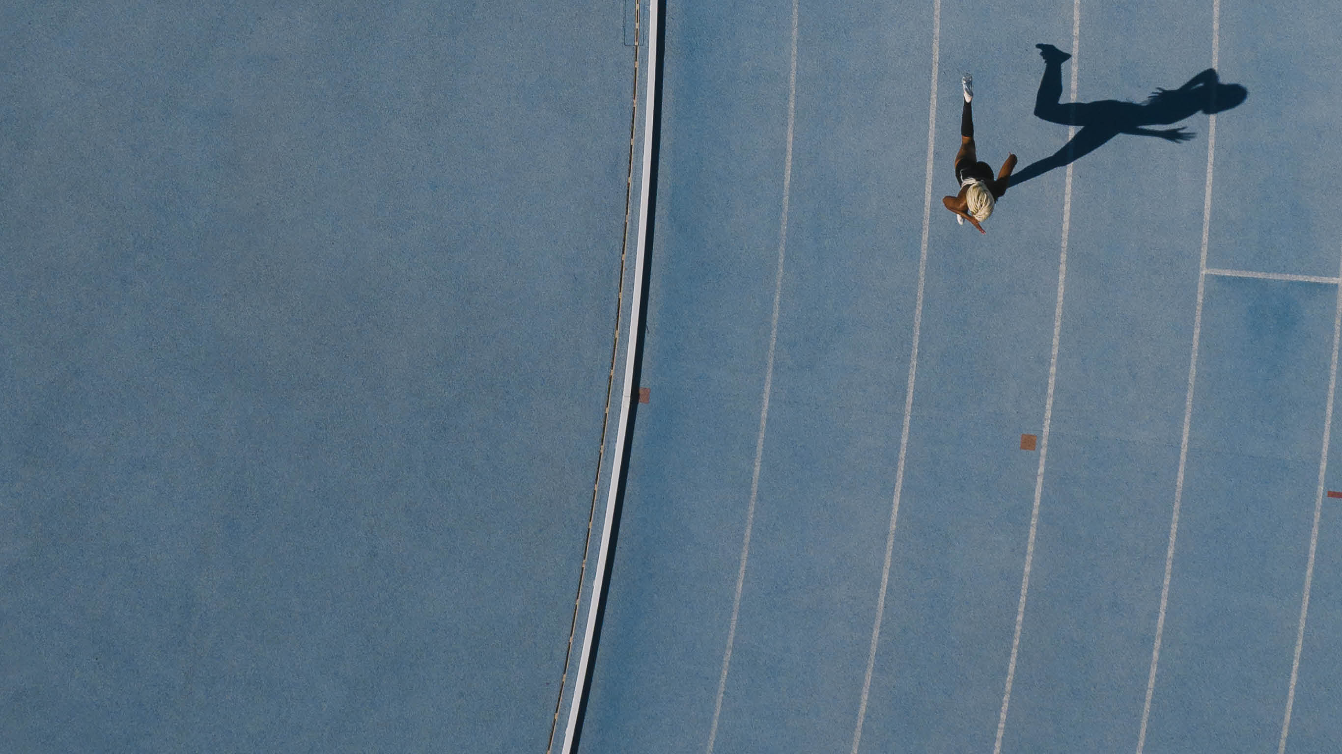 Sprinter running on athletic track  Top view of a sprinter running on race track in a stadium with shadow falling on the side 