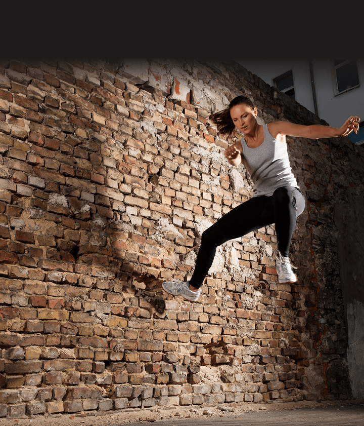 Young woman Tic-Tacing off a wall to change direction while doing Free-Running Parkour in an urban area  Horizontal shot 