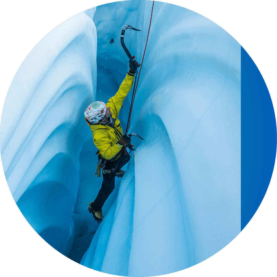 Ice climber ascending a narrow passage inside a glacier ice cave with wavy lines from melting ice cutting into the walls 