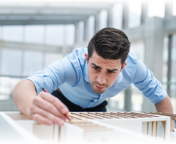 Young businessman or architect with model of a house standing at the desk in office, working 